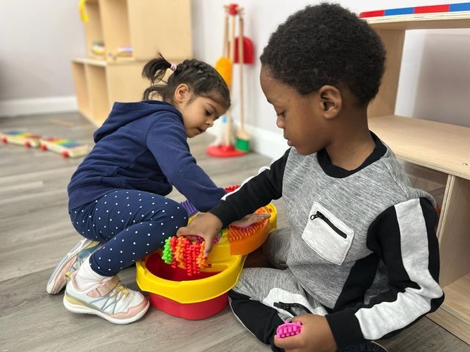 Two young children playing with colorful toys in a classroom setting.