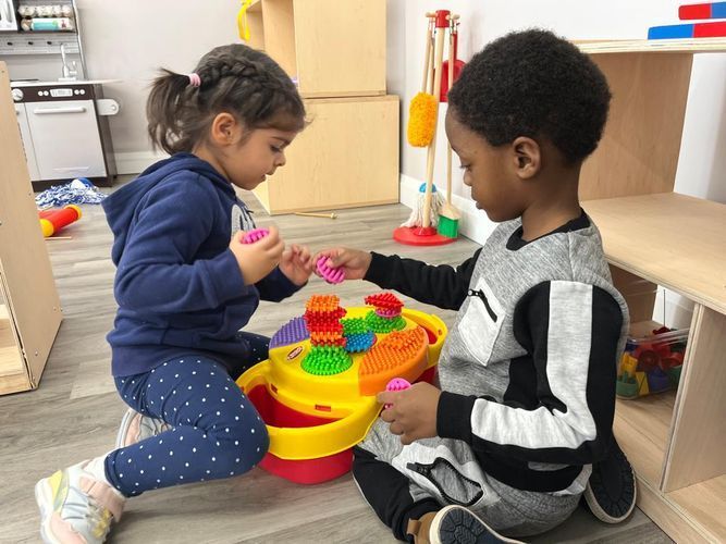 Two young children playing with a colorful stacking toy indoors.