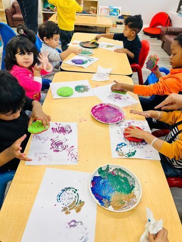 Children at tables do printmaking with colorful paint and sponges.