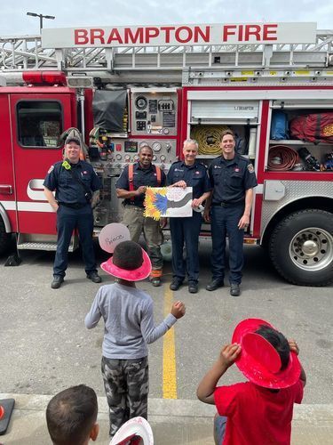 Firefighters with fire truck pose with children holding a painting, Brampton, Ontario.