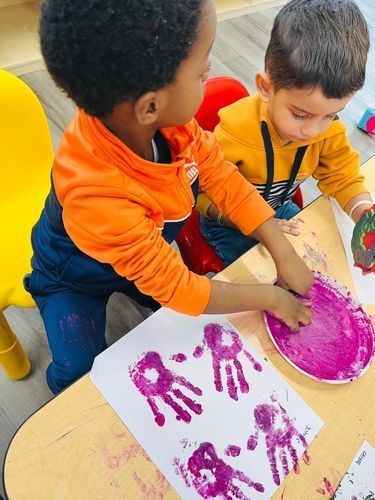 Two young children making handprint art with pink paint at a table.