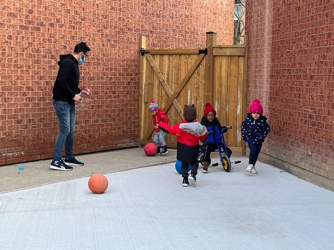 Man in mask plays basketball with four children in a brick-walled courtyard.