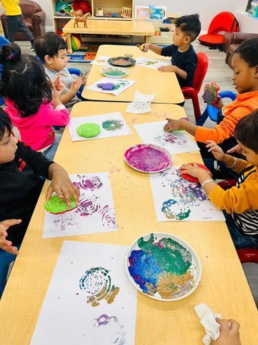 Children in classroom, doing art project, using paint stamps on paper.