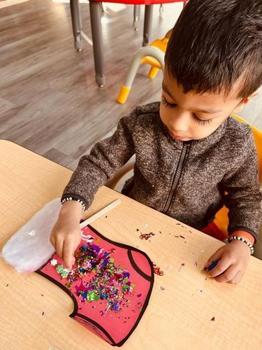 Boy at table decorates paper craft with glitter and other materials.