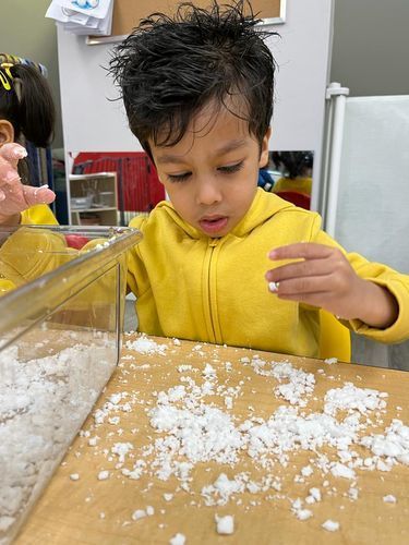 Boy in yellow jacket looks intently at play snow.