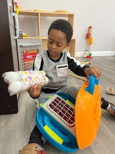Young Black child playing with toy food and refrigerator, sitting on a floor.