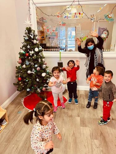 Children and a teacher waving near a Christmas tree in a brightly lit room.