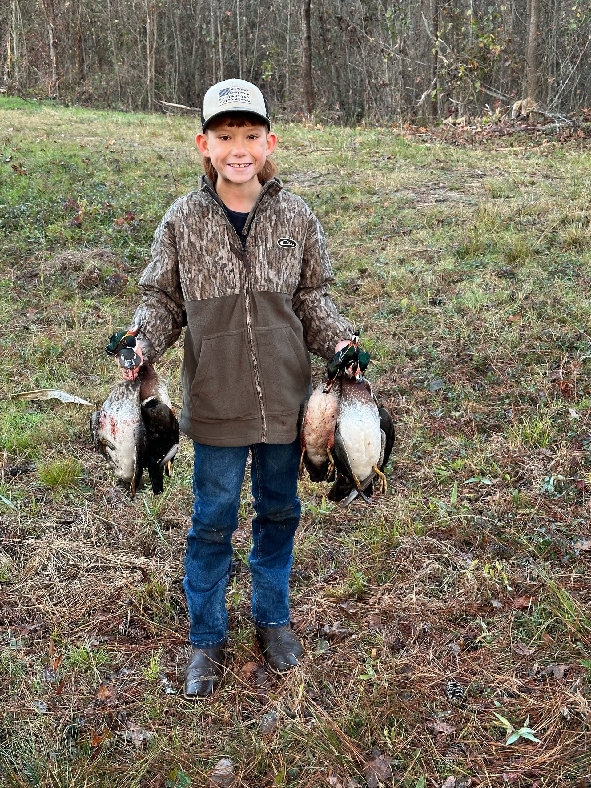 A young boy is holding two ducks in a field.