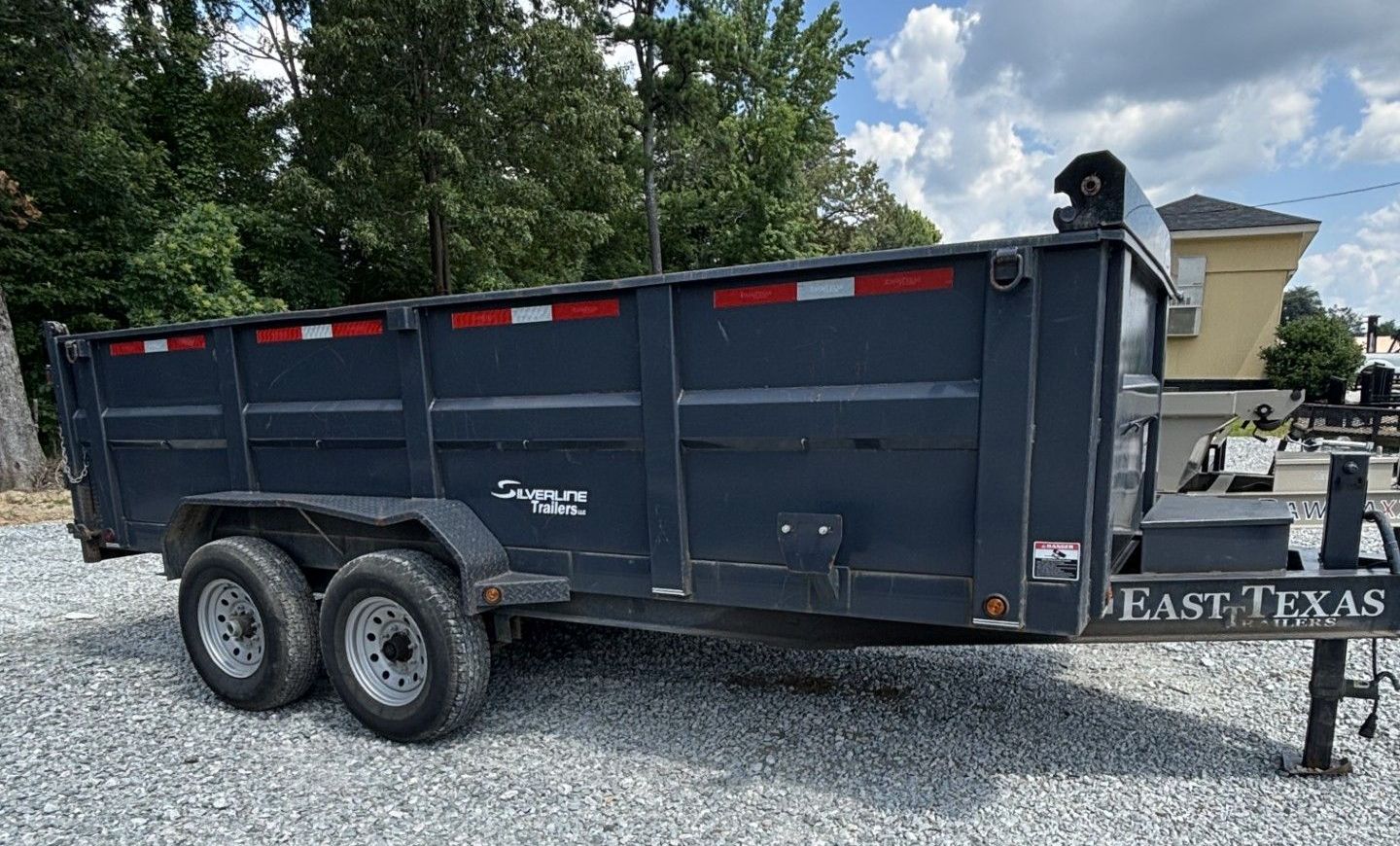 A flatbed trailer with a wooden deck is parked in a gravel lot.