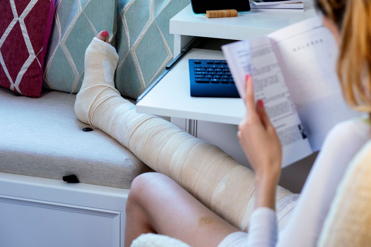 Woman with leg cast reading, seated indoors near a small table with a keyboard.