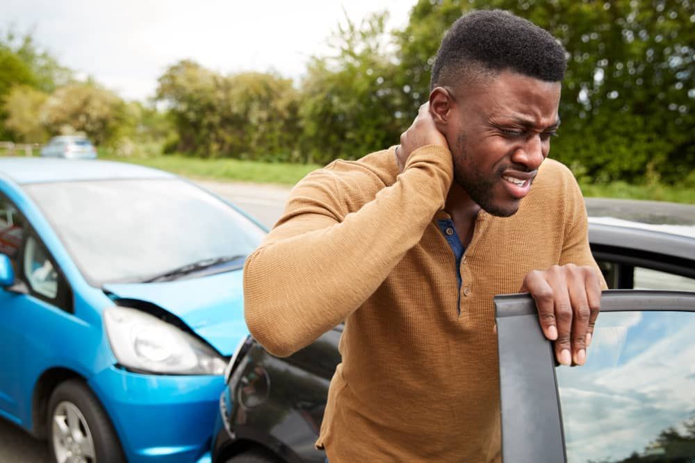 Man holding neck, grimacing near damaged cars after a car accident.