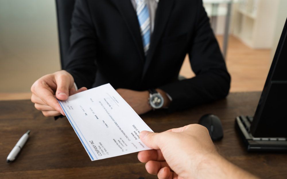 A man in a suit and tie is handing a check to another man.