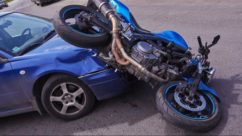 A motorcycle has crashed into a blue car on the side of the road.