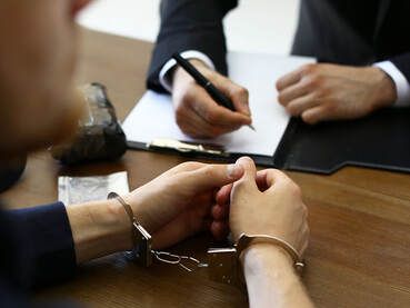 A man in handcuffs is sitting at a table with a lawyer.