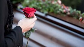 A woman is holding a red rose in front of a coffin.