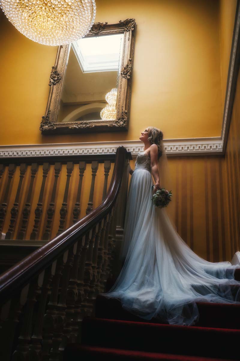 Fitzgeralds Vienna Woods wedding photo - bride at stairs landing with hanging chandelier above 
