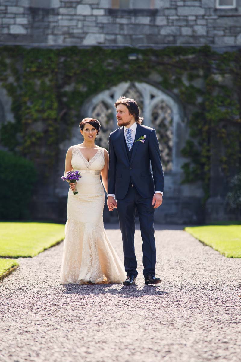 wedding couple holding hands and walking along stone path at Honan Chapel UCC