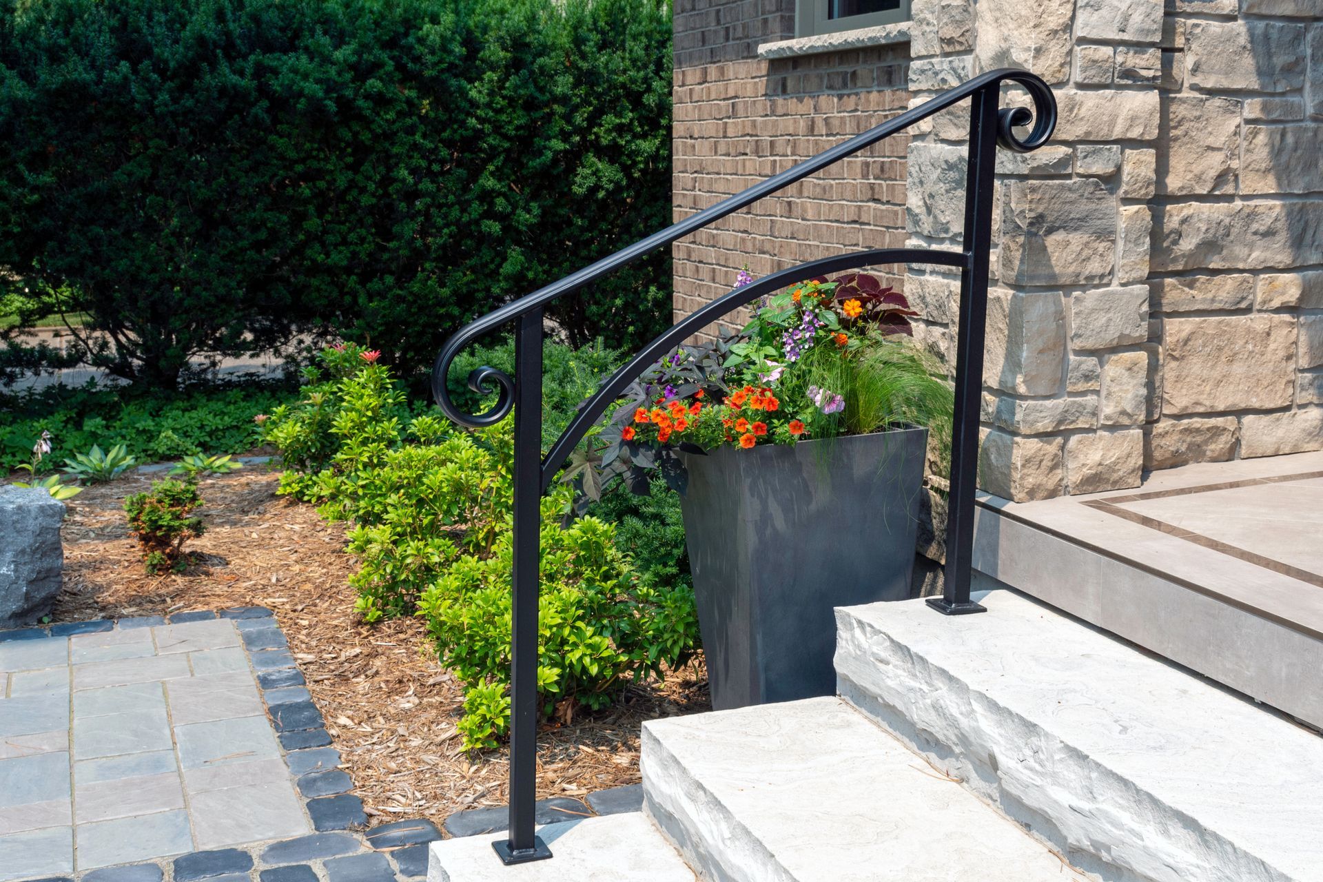 A wrought iron railing on a set of stairs next to a planter of flowers.