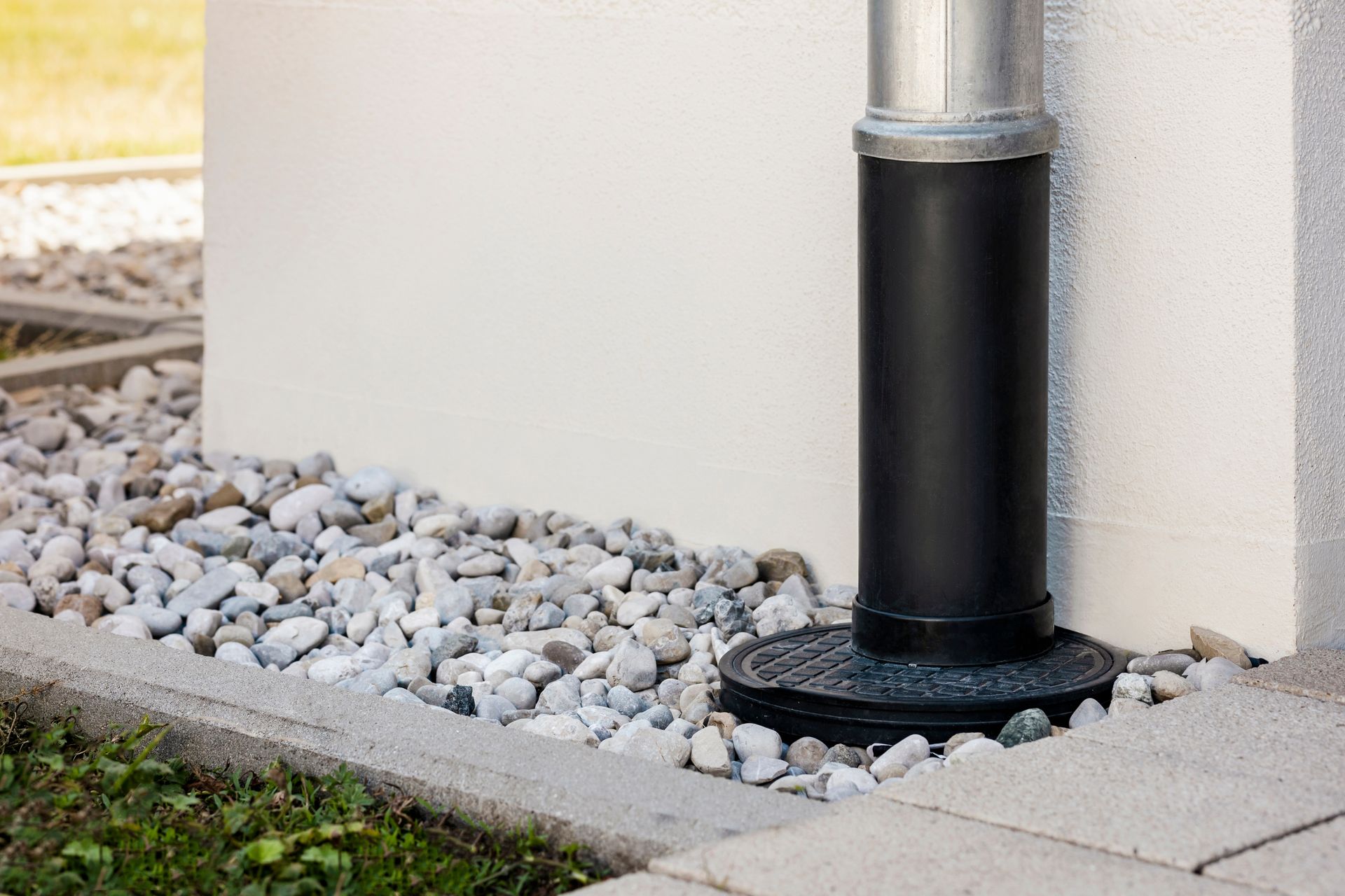 A black drainpipe is sitting next to a white wall.