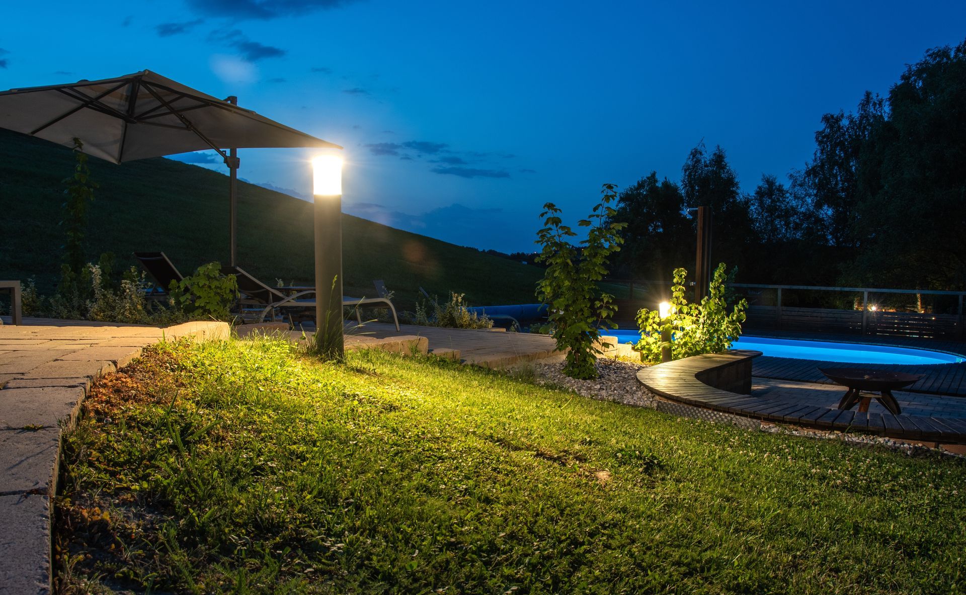 A lawn with a umbrella and a pool at night.