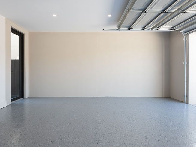 An empty garage with a garage door open and a gray floor.