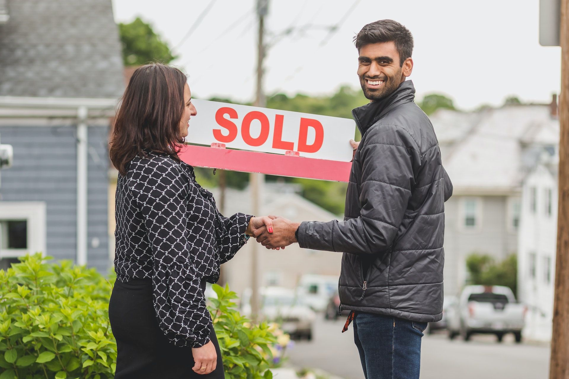 man shaking hands with woman real estate agent holding sold sign