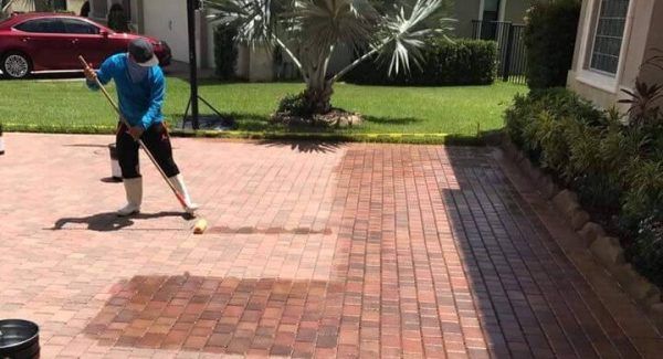 A man is cleaning a brick driveway with a broom.