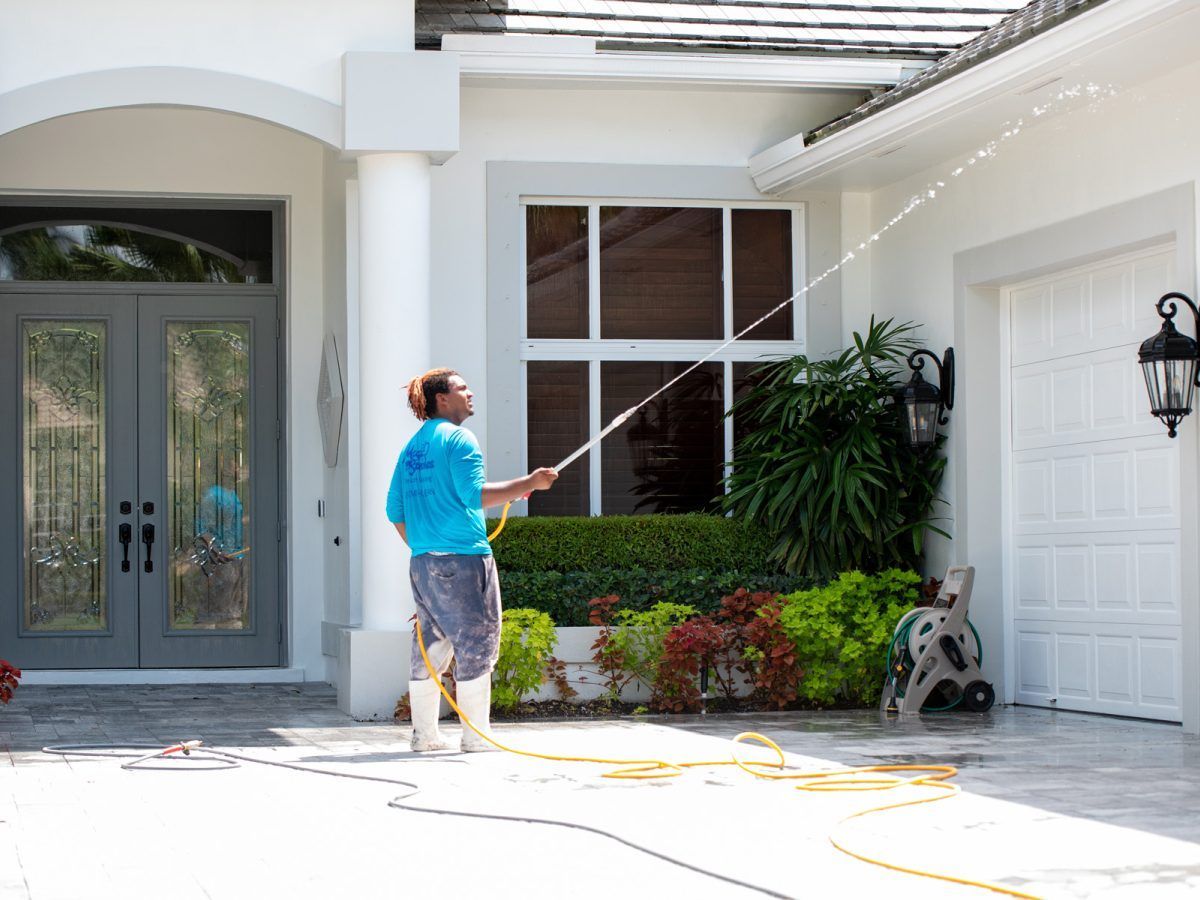 A man is cleaning a white house with a hose.