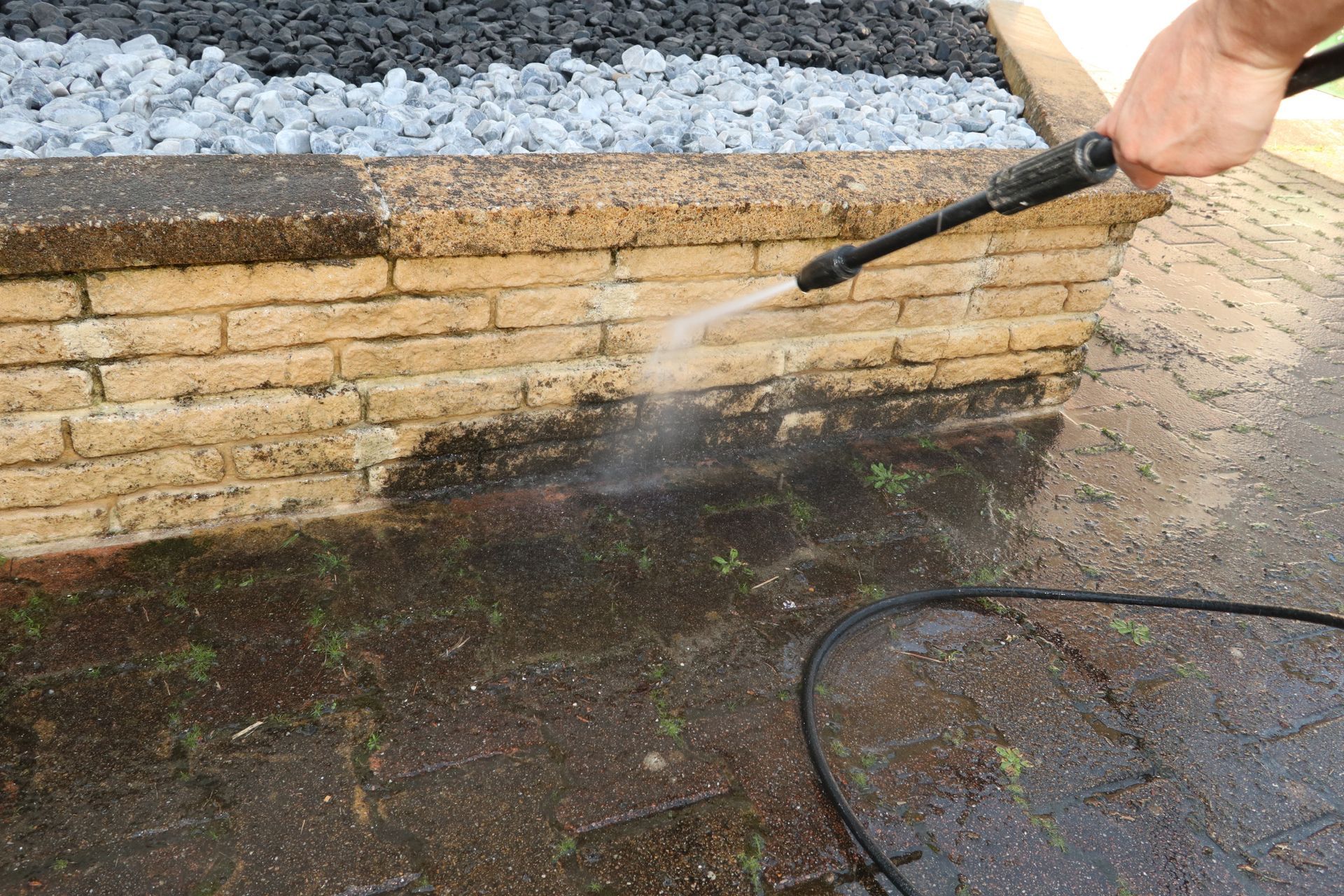 A person is using a high pressure washer to clean a brick wall.