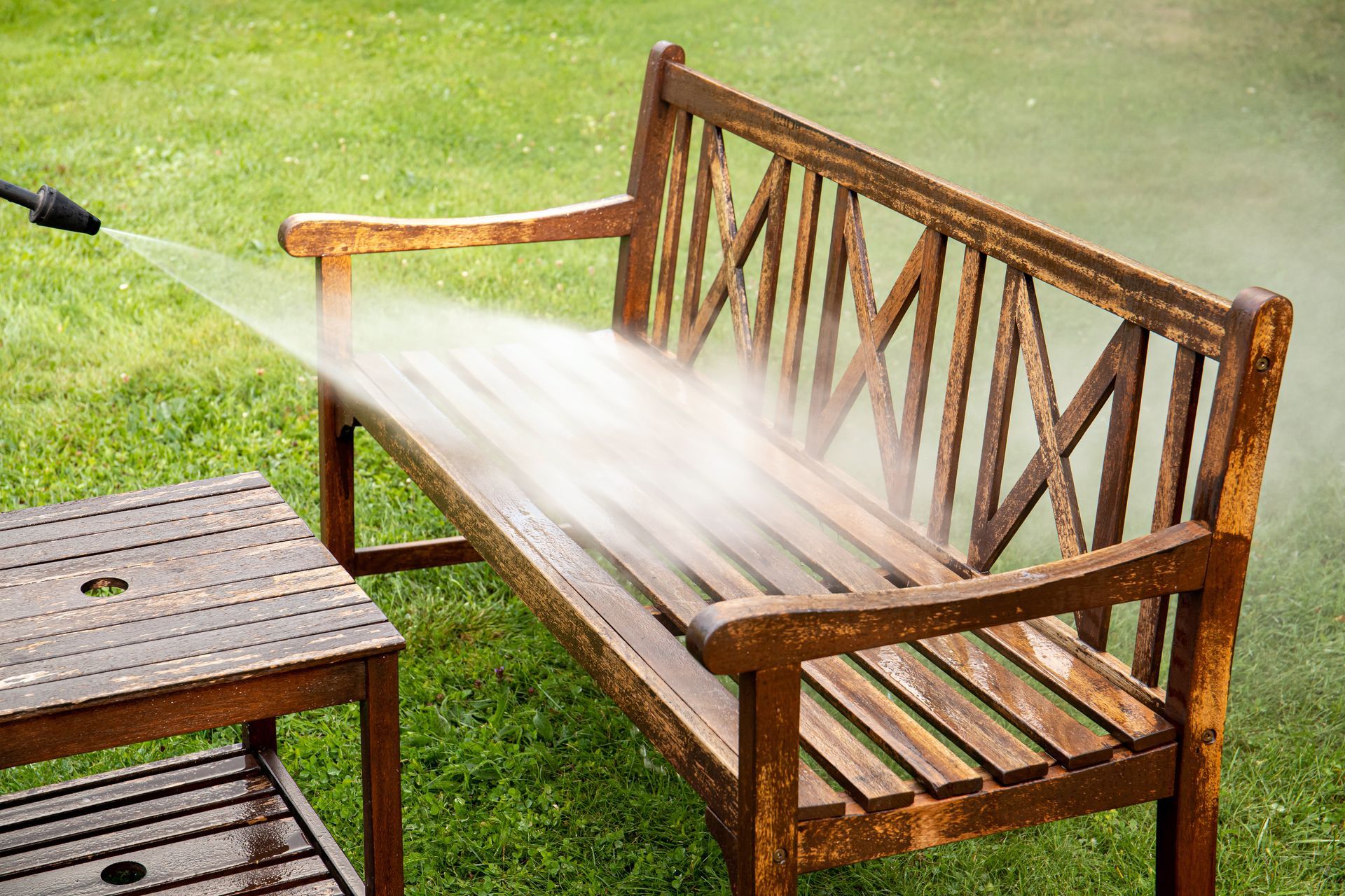 A person is cleaning a wooden bench with a high pressure washer.