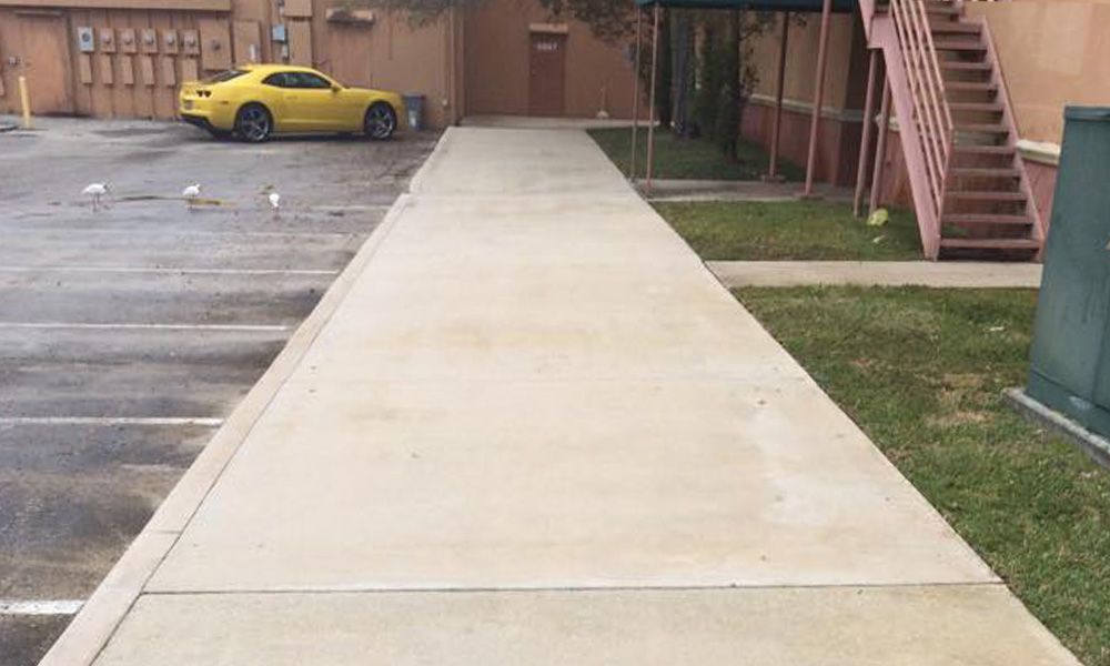 A yellow car is parked in a parking lot next to a sidewalk.