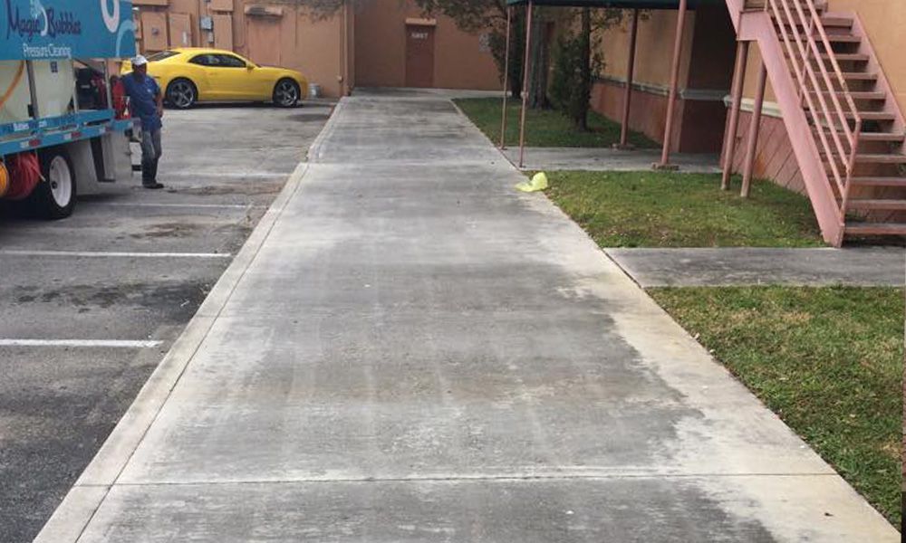 A man is cleaning a concrete sidewalk in front of a building.