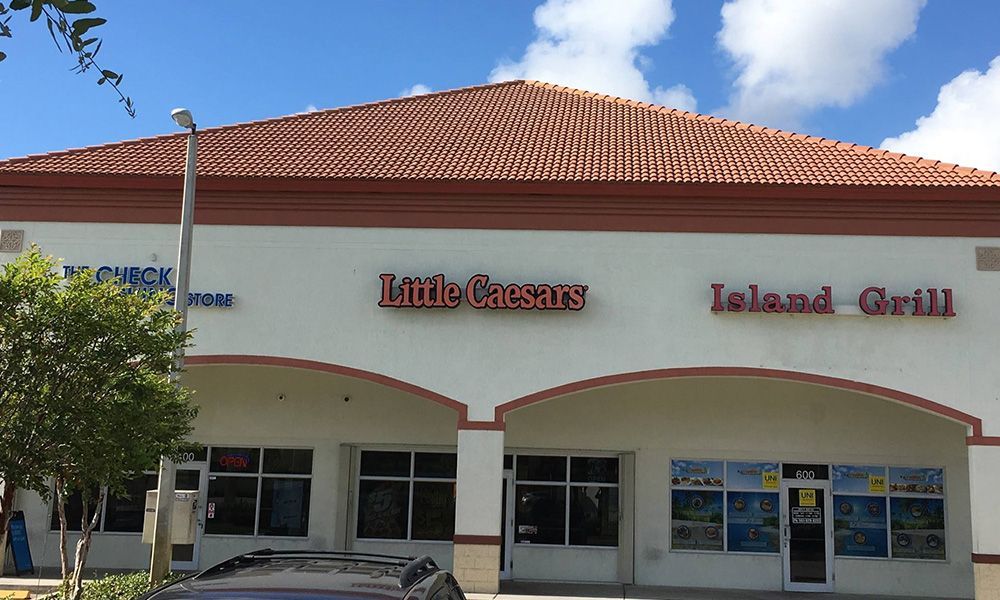 The front of a little caesars restaurant with a car parked in front of it.