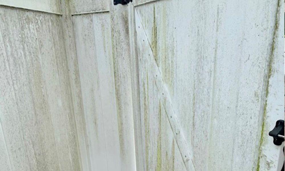 A white fence with green algae growing on it.