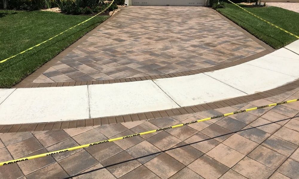 A brick driveway with a white curb and a yellow tape.