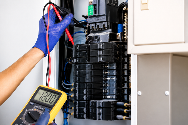 Gloved electrician testing a circuit breaker panel with a multimeter.
