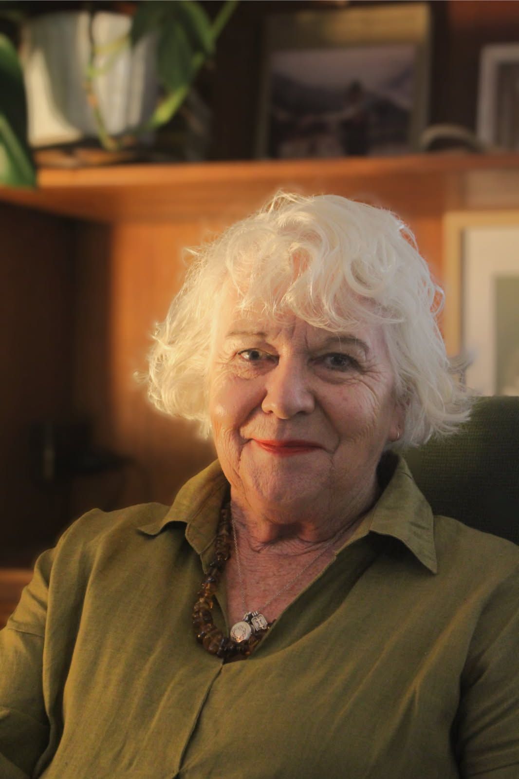 Portrait of an older woman with curly white hair, wearing a dark shirt, looking off to the side in warm light