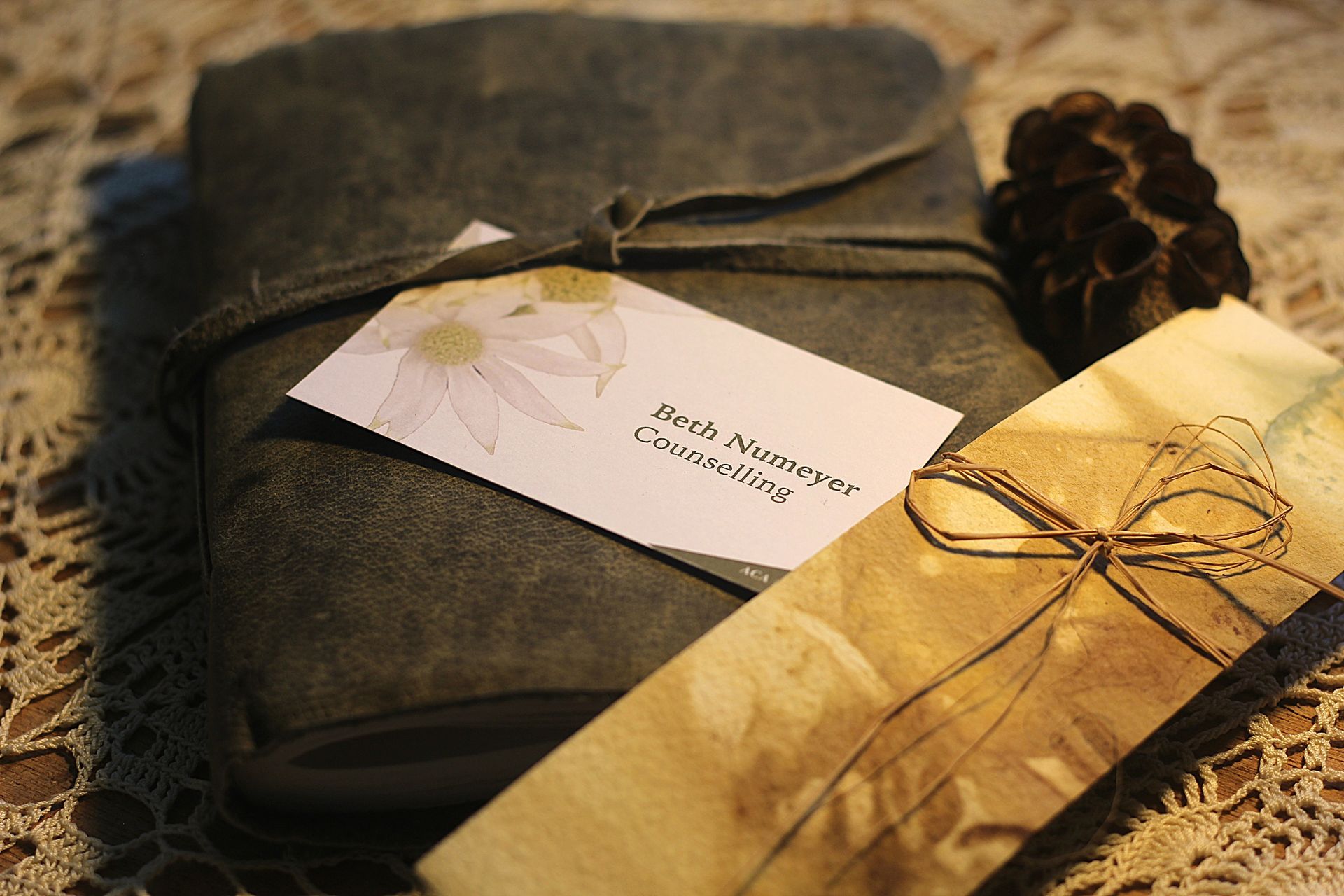 Gift-wrapped stationery set with a gold card, dark notebook, twine bow, and pinecone on burlap