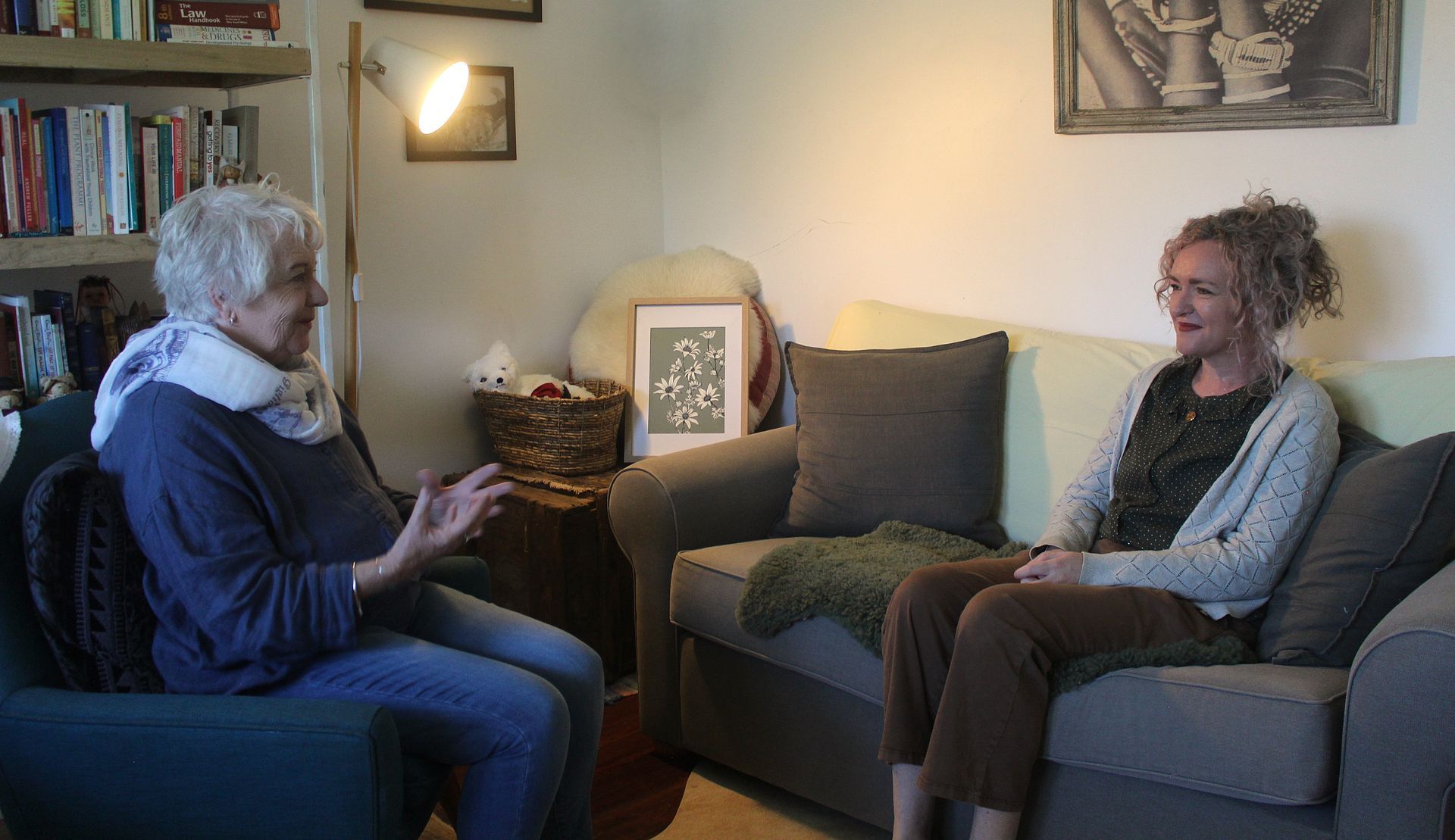 Two people sitting and talking in a cozy living room with gray chairs and warm lighting