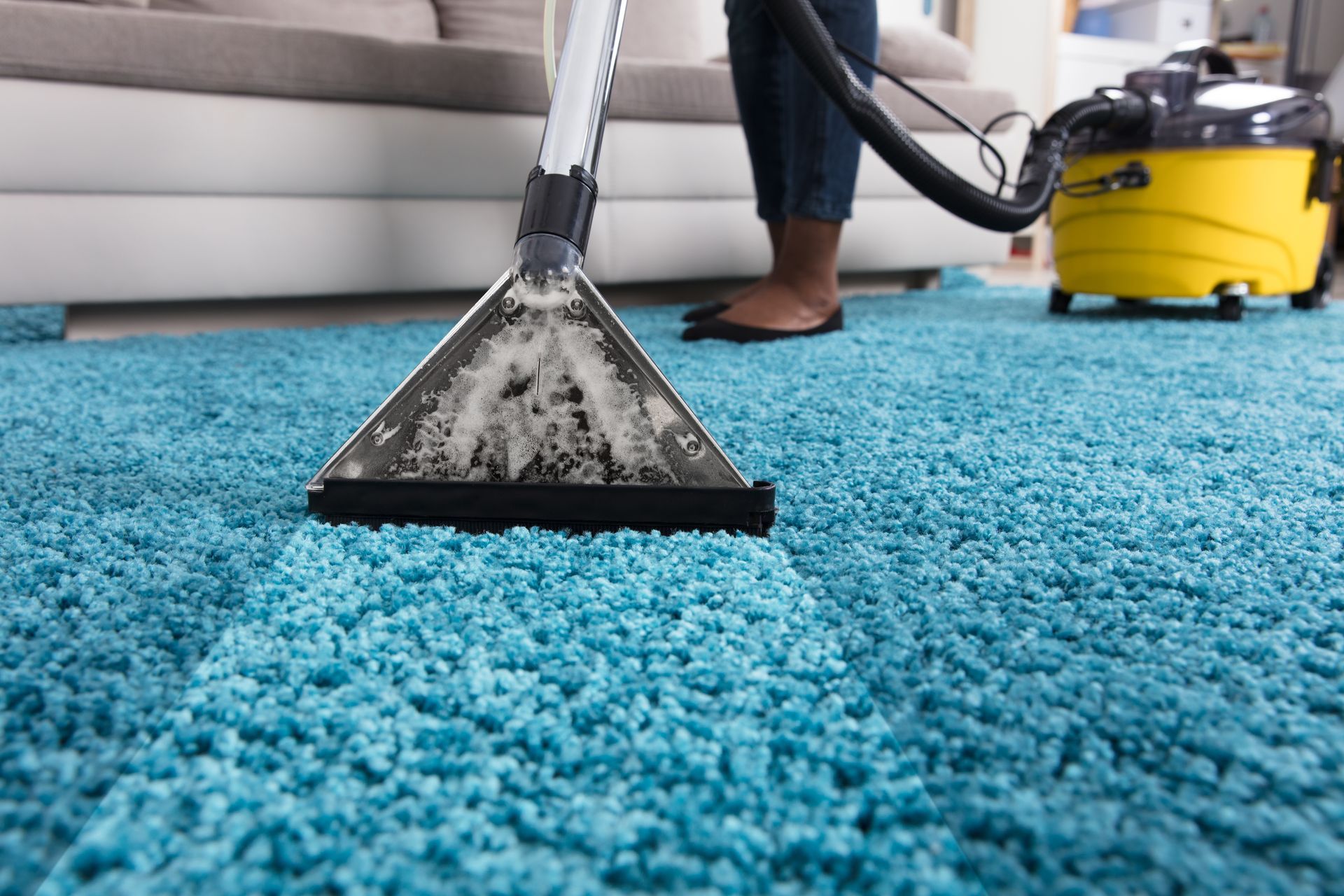 A person uses a yellow carpet cleaning machine to clean a bright blue shag rug.
