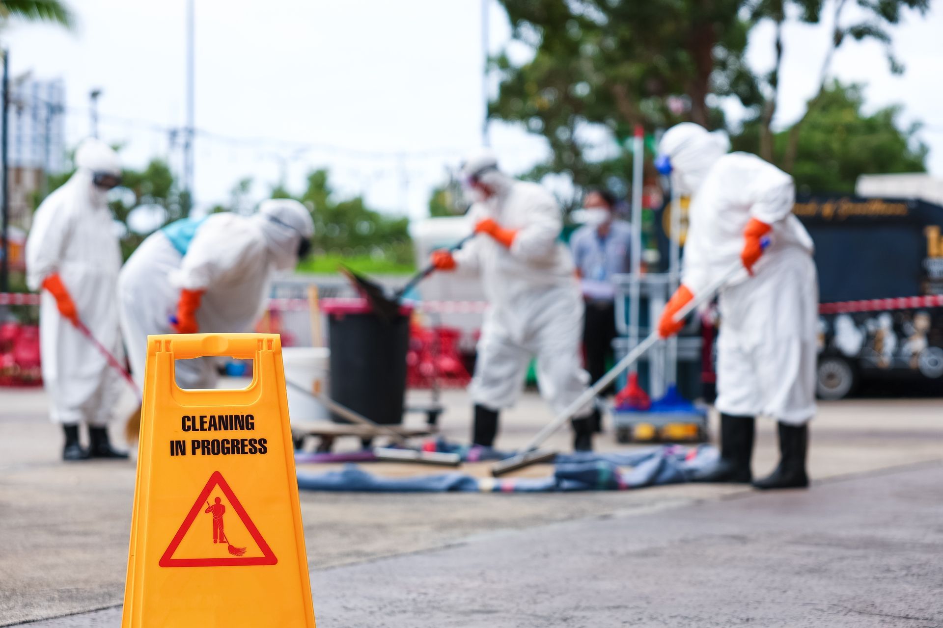 Workers in white protective suits clean an outdoor area near a yellow
