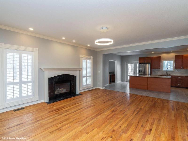 An empty living room with hardwood floors , a fireplace , and a kitchen.