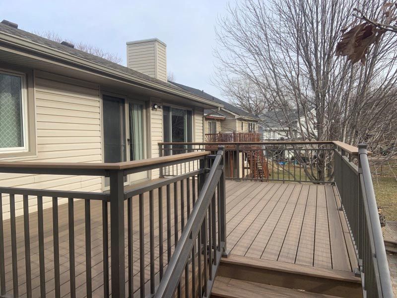 A wooden deck with a metal railing is in front of a house.