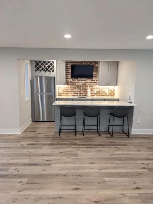 A kitchen with stools , a refrigerator , and a brick wall.