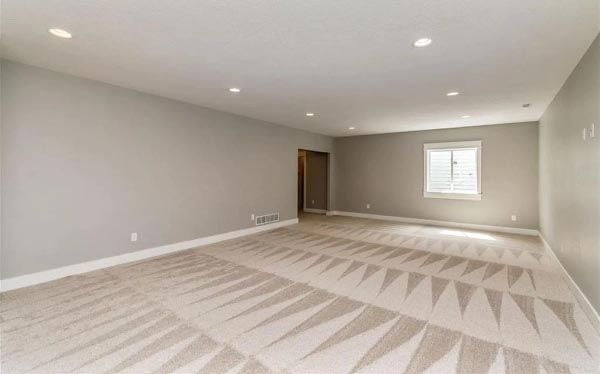 A large empty room with a carpeted floor and a window.