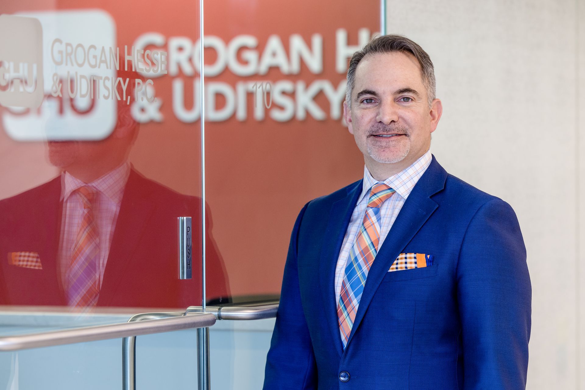 A man in a suit and tie is standing in front of a glass wall.