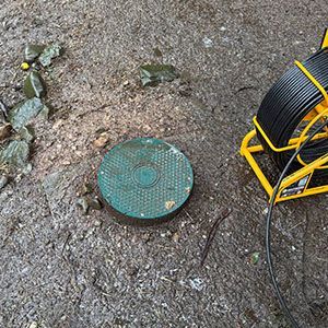 Round green utility cover in muddy ground beside a yellow cable reel.