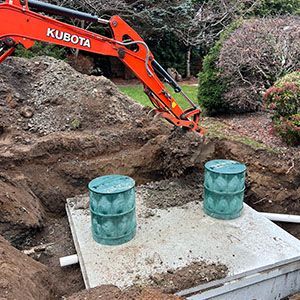Orange Kubota excavator digging beside a concrete slab with two green barrels outdoors