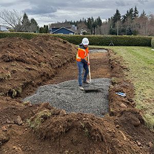 Worker in orange vest leveling gravel in a long trench at a construction site