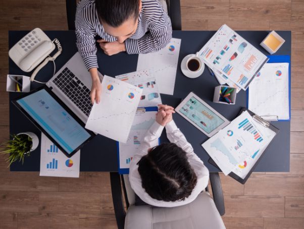 A man and a woman are sitting at a desk with papers and a laptop.